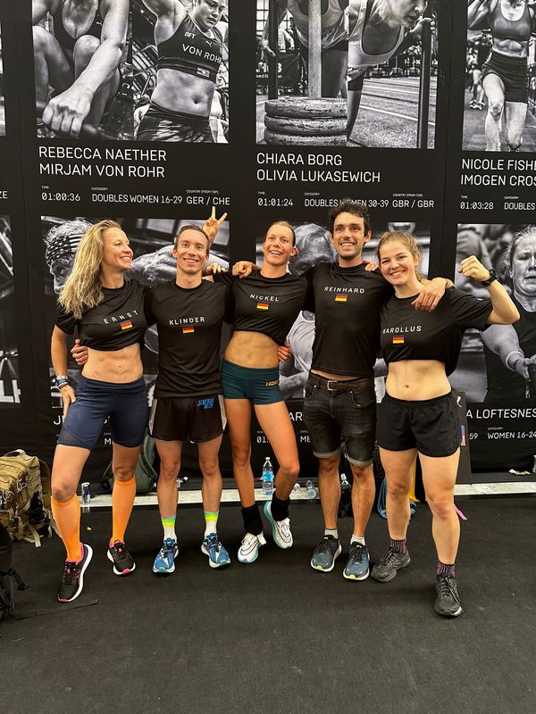 Fünf Athletinnen und Athleten im Nationalteam-Shirt vor der Porträtwand der Hyrox-WM in Nizza