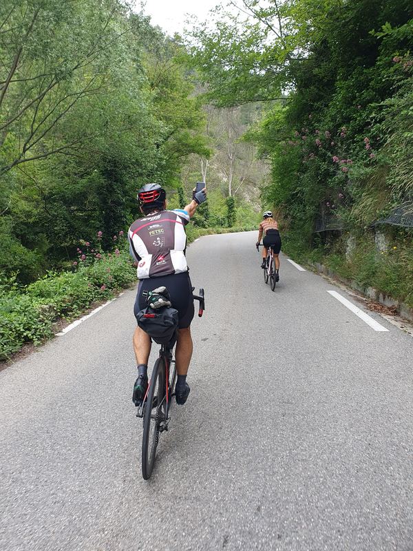 Radfahrerin im orangen Trikot fährt vor uns durch eine grüne Schlucht