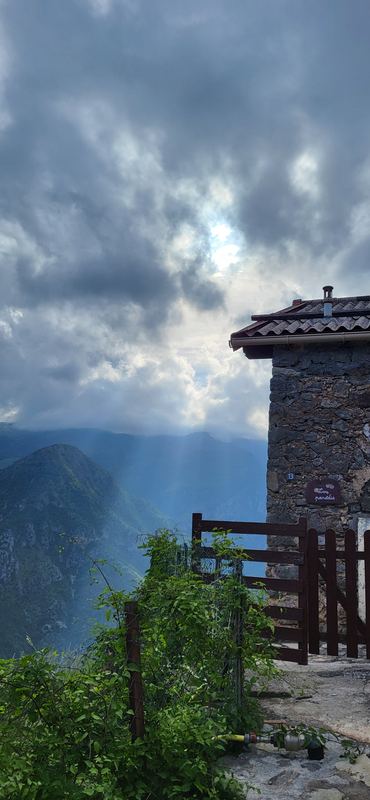 Steinhaus am Dorfrand, Sonnenstrahlen fallen durch Wolken ins Tal
