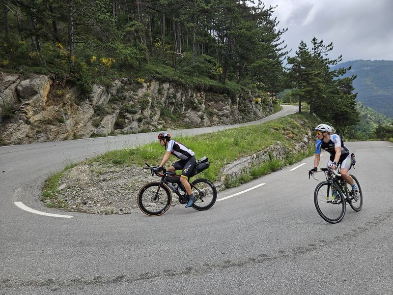 Zwei Radfahrer mit Gepäck in einer engen Kehre vor Felswand und Pinien