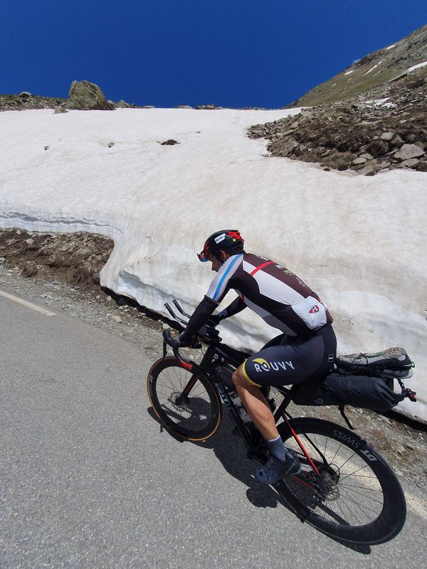 Radfahrer mit Gepäck fährt an einer zwei Meter hohen Lawinen-Schneewand vorbei