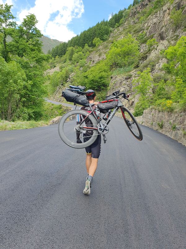 Rennrad mit Gepäck auf der Schulter, zu Fuß auf frisch asphaltierter Straße