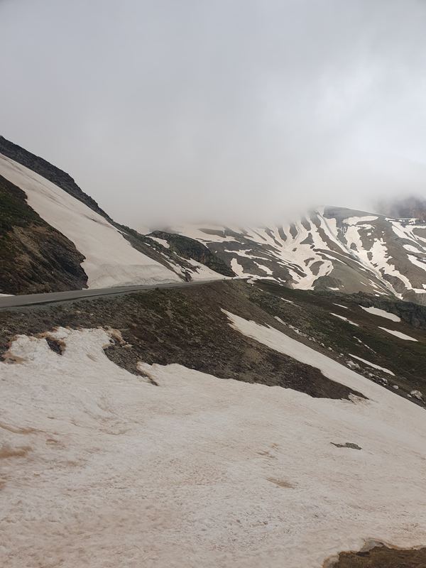 Straße zwischen Schneefeldern am Galibier, der Grat verschwindet im Nebel
